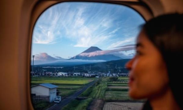 A woman looks out of the window of a bullet train at Mount Fuji